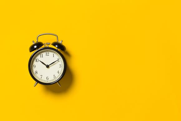 A black analog alarm clock on a yellow background.