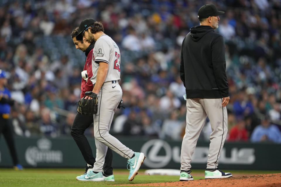 Arizona Diamondbacks starting pitcher Zac Gallen leaves with a trainer as manager Torey Lovullo, right, stands on the mound during the sixth inning of the team's baseball game against the Seattle Mariners, Friday, April 26, 2024, in Seattle. (AP Photo/Lindsey Wasson)