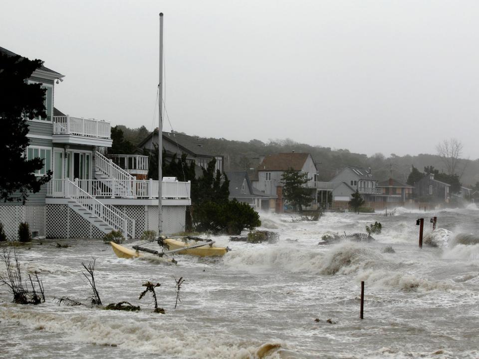 white waves of ocean water crash into shoreline with homes and boats