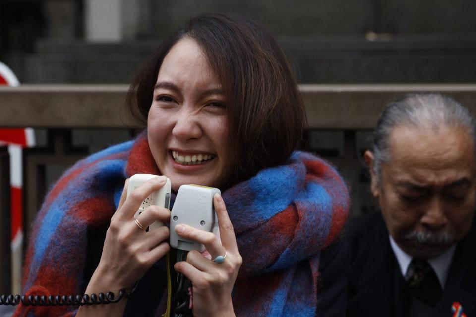 Woman stands smiling and crying while holding two microphones