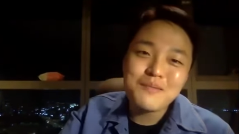 Do Kwon looking at the screen and smiling amid a background of city lights.