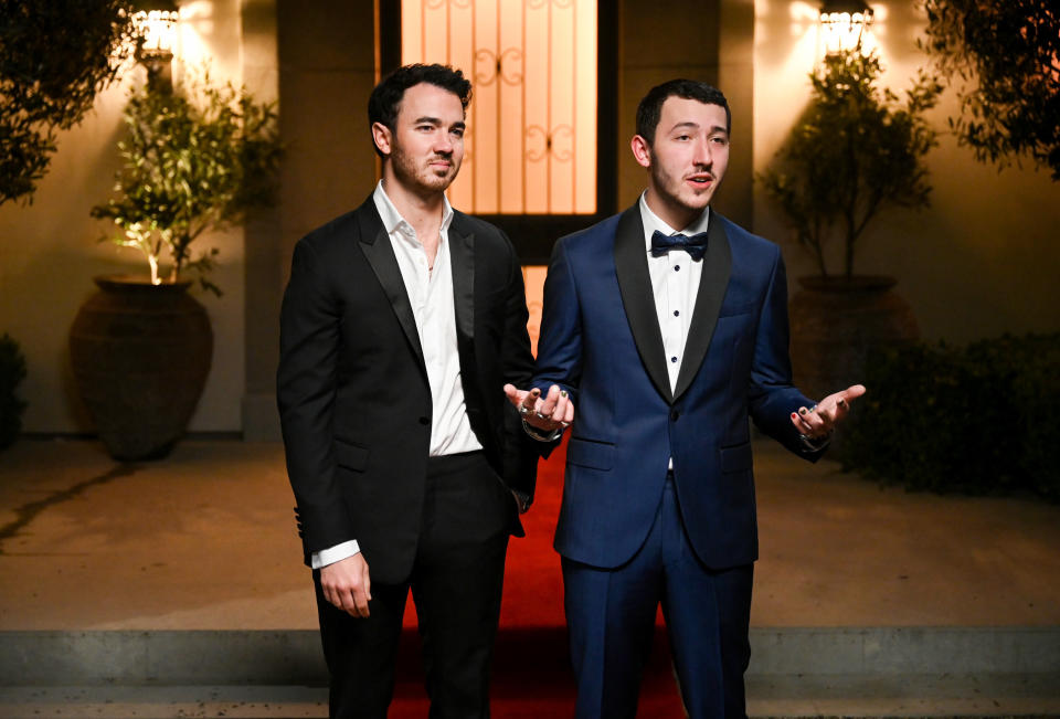 Wearing a suit and bow tie and standing with one of his brothers