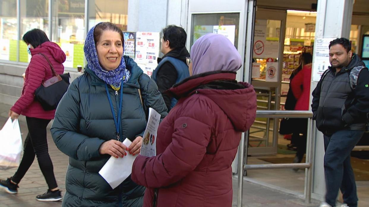 Health ambassadors Eshrat Meshkat, left, and Hafsa Fatima hand out flyers for a Ramadan health workshop outside of Sunny Foodmart in Flemingdon Park. Community health workers say ambassadors have become central to the wellbeing of residents. (Derek Hooper/CBC - image credit)