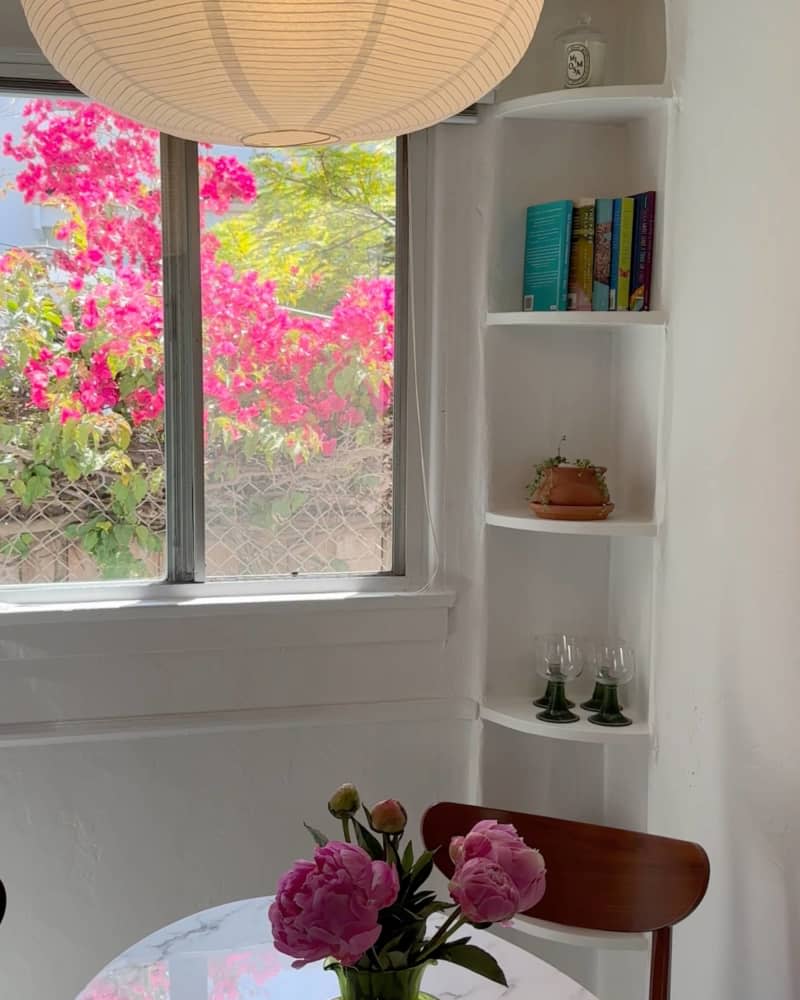 Paper mache oval lighting fixture, arched corner built in book case, round white table with dark wood mid-century modern chairs