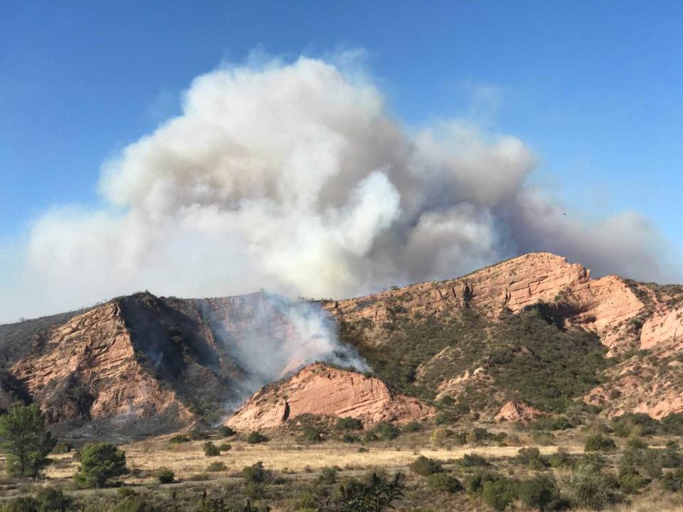 A large plume rises from behind rugged terrain along Santiago Canyon Road, where the Bond fire continues to burn.