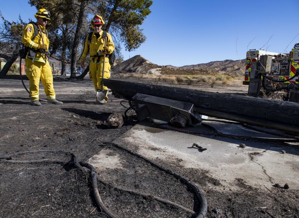 Firefighters with Cal Fire examine a burned down low voltage power pole during the Tick Fire, Thursday, Oct. 25, 2019, in Santa Clarita, Calif. An estimated 50,000 people were under evacuation orders in the Santa Clarita area north of Los Angeles as hot, dry Santa Ana winds howling at up to 50 mph (80 kph) drove the flames into neighborhoods (AP Photo/ Christian Monterrosa)