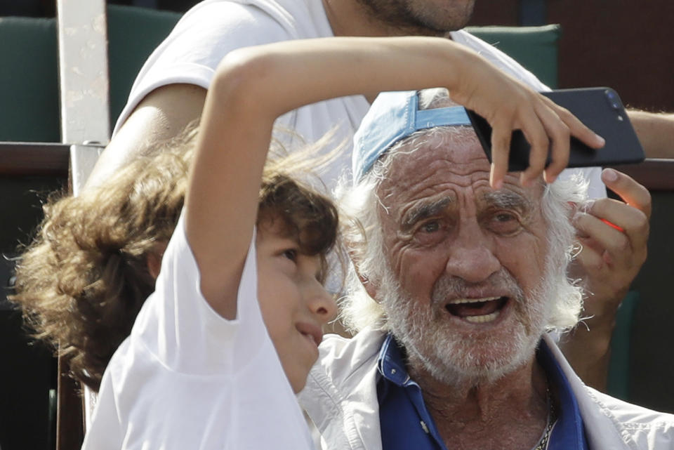 FILE - In this June 8, 2018 file photo, a child takes a selfie with French actor Jean-Paul Belmondo during the semifinal match at the French Open tennis tournament between Spain's Rafael Nadal and Argentina's Juan Martin Del Potro at the Roland Garros stadium in Paris. French New Wave actor Jean-Paul Belmondo has died, according to his lawyer’s office on Monday Sept. 6, 2021. (AP Photo/Alessandra Tarantino, File)