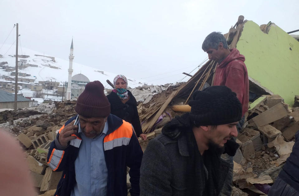 People stand on the debris of their collapsed house after an earthquake hit villages in Baskale town in Van province, Turkey, at the border with Iran, Sunday, Feb. 23, 2020. Turkish Interior Minister Suleyman Soylu said numerous people have been killed and several others wounded in Sunday's quake.(DHA via AP)