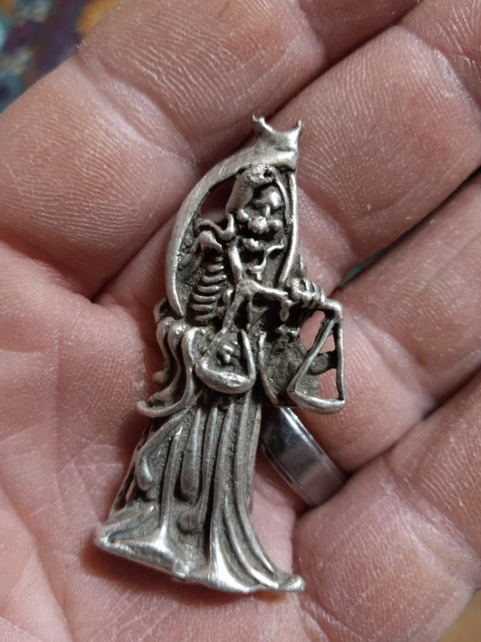 Silver pendant with intricate design of a figure playing a harp, held in a person's hand