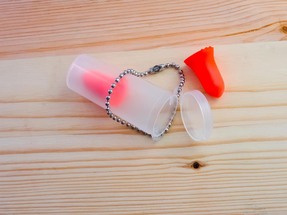 Red earplugs by plastic container on light wood table