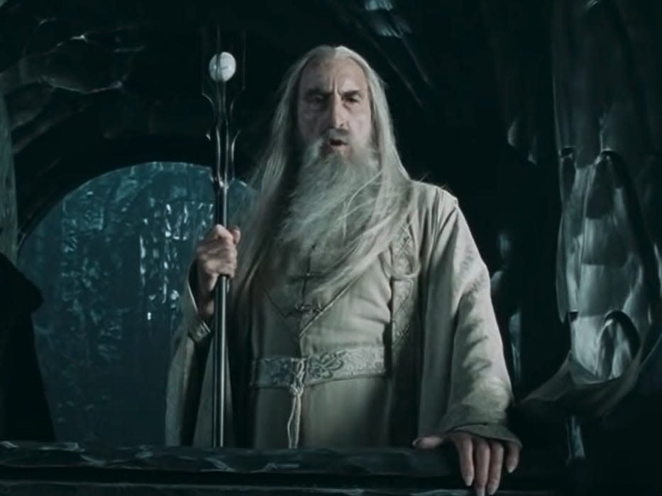 Saruman wearing a white outfit and holding a staff in lord of the rings