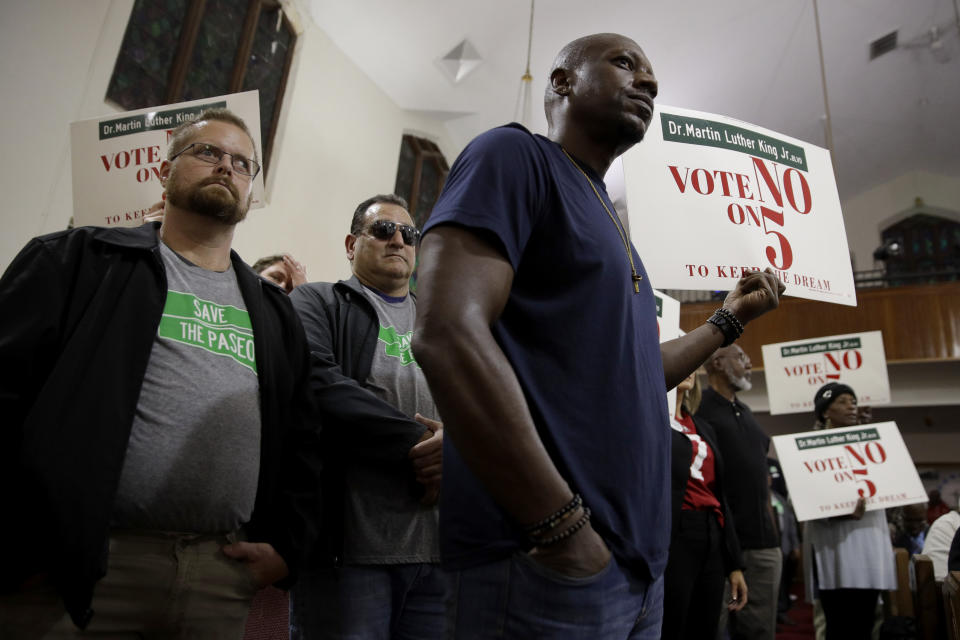 In this Sunday, Nov. 3, 2019, photo, people wearing "Save The Paseo" shirts stand among attendees at a rally to keep a street named in honor of Dr. Martin Luther King Jr. at Paseo Baptist Church in Kansas City, Mo. In January, the City Council voted to rename one of the city's main boulevards, The Paseo, after King, but many in the community want the old name back. A petition drive put the issue on the Nov. 5 ballot pitting neighbors against each other. (AP Photo/Charlie Riedel)