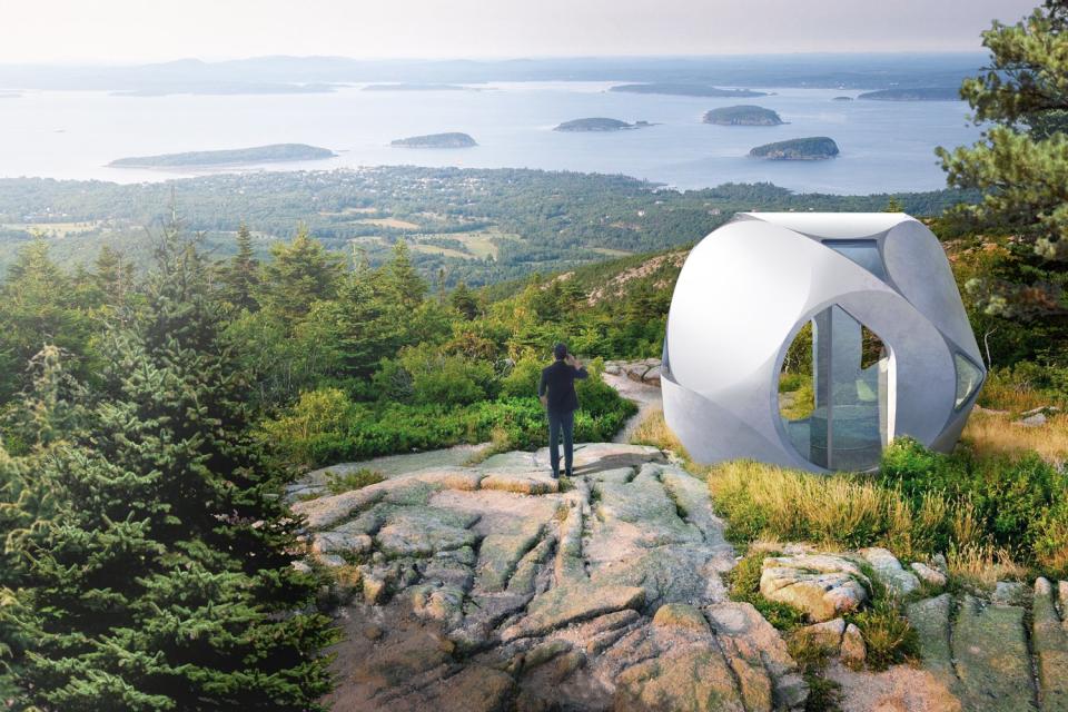 Man stands beside a Serendix Partners' 3D-printed housing pod atop a hill. 