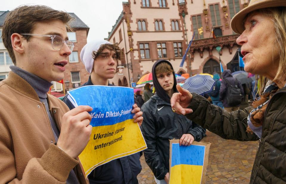 People holding blue and yellow posters stand in the rain.