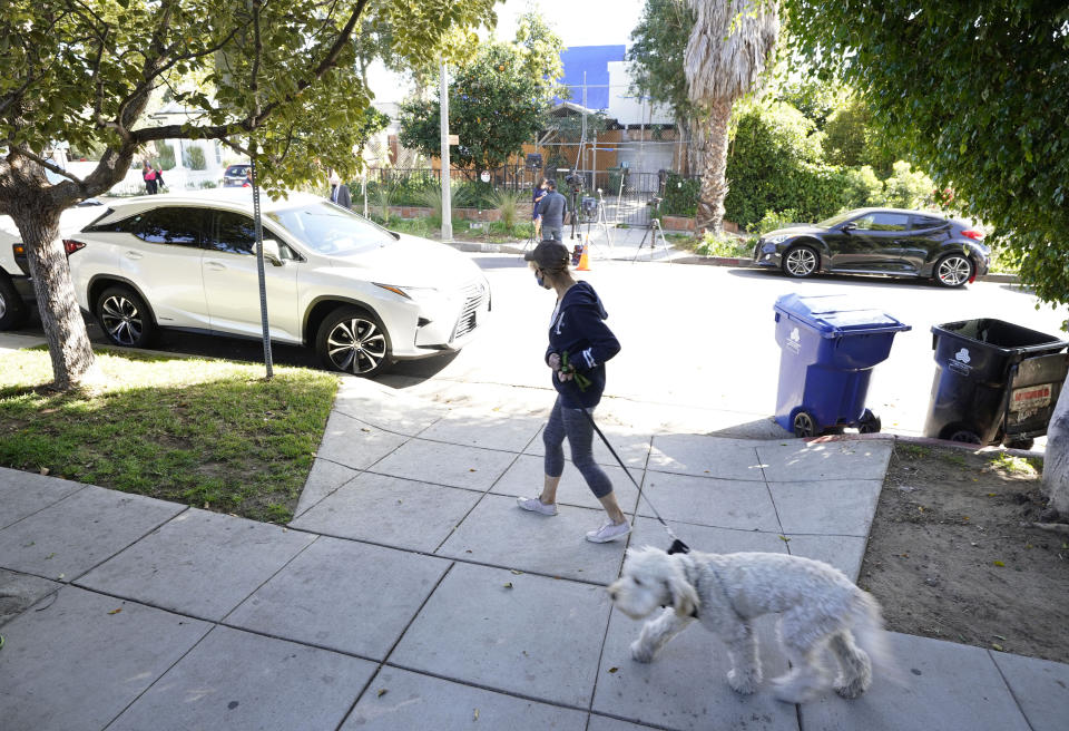 A woman walks her dog across the street from an area on North Sierra Bonita Ave. where Lady Gaga's dog walker was shot and two of her French bulldogs stolen, Thursday, Feb. 25, 2021, in Los Angeles. The dog walker was shot once Wednesday night and is expected to survive his injuries. The man was walking three of Lady Gaga's dogs at the time but one escaped. (AP Photo/Chris Pizzello)