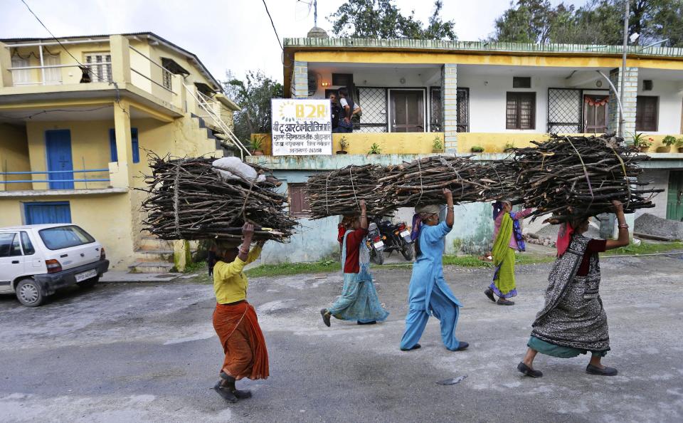 In this Aug. 23, 2012 photo, women carrying bundles of wood on their head walk past the offices of B2R in Simayal, India. Before B2R arrived in Simayal, local women had little option but to marry right out of school, and educated young men had to travel far to seek respectable jobs. (AP Photo/Saurabh Das)