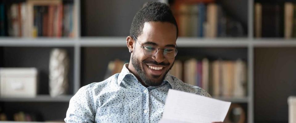 Happy smiling African American man wearing glasses reading letter.