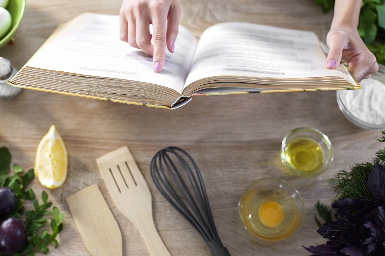 woman reading recipe in culinary book at home with kitchenware on table