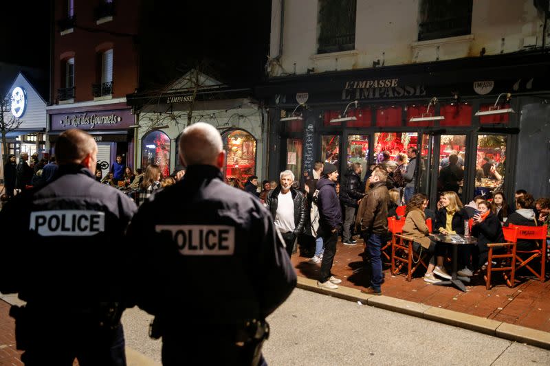 Policemen stand guard while people enjoy dinner and drinks before the French Prime Minister Edouard Philippe's announcement of the shutdown of non-essential commerce and places takes effect in France at midnight, in Le Touquet