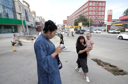 A woman and a boy look at Li Doudou dressed in "Hanfu", as she waits for a taxi to attend a performance of the "guqin" traditional musical instrument, in Hebei province, China