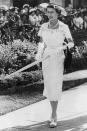 <p>In a garden wearing a fitted floral dress, white peep toe sandals, a pearl necklace, sun hat, and an umbrella. </p>