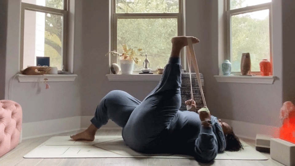 Woman stretching hamstrings while lying on her back in her bedroom