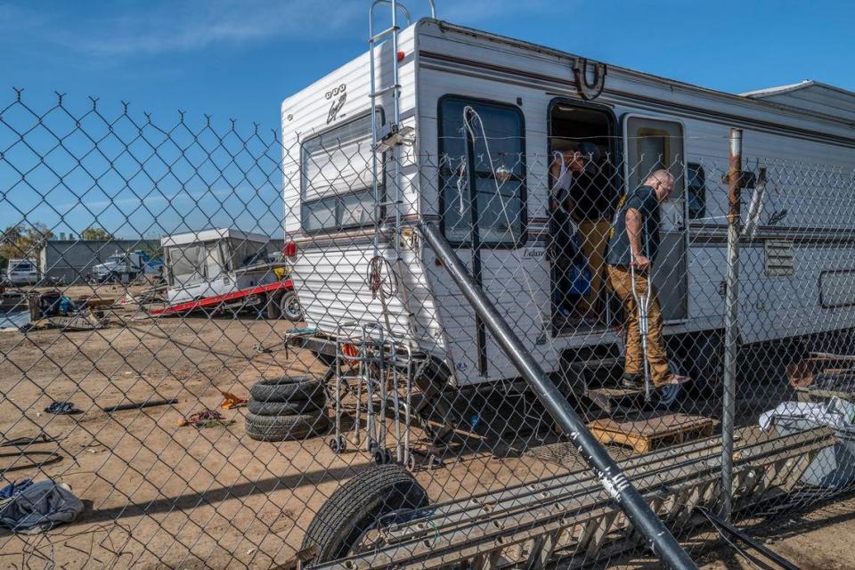 Harry Avis, 51, who said he injured his leg in a motorcycle accident a few weeks ago, uses crutches as he exits his travel trailer parked in a homeless encampment near Lexington Street and Dixieanne Avenue in Old North Sacramento on Wednesday, May 25, 2022. At left, city crews load a small white structure that belonged to another homeless camper onto a flatbed truck.