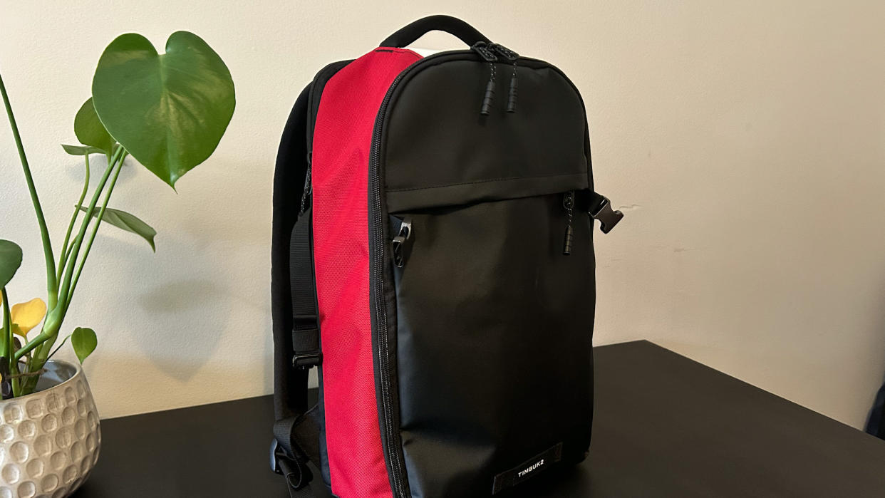  Timbuk2 Division backpack in red, white and black sitting on a black table next to a plant 