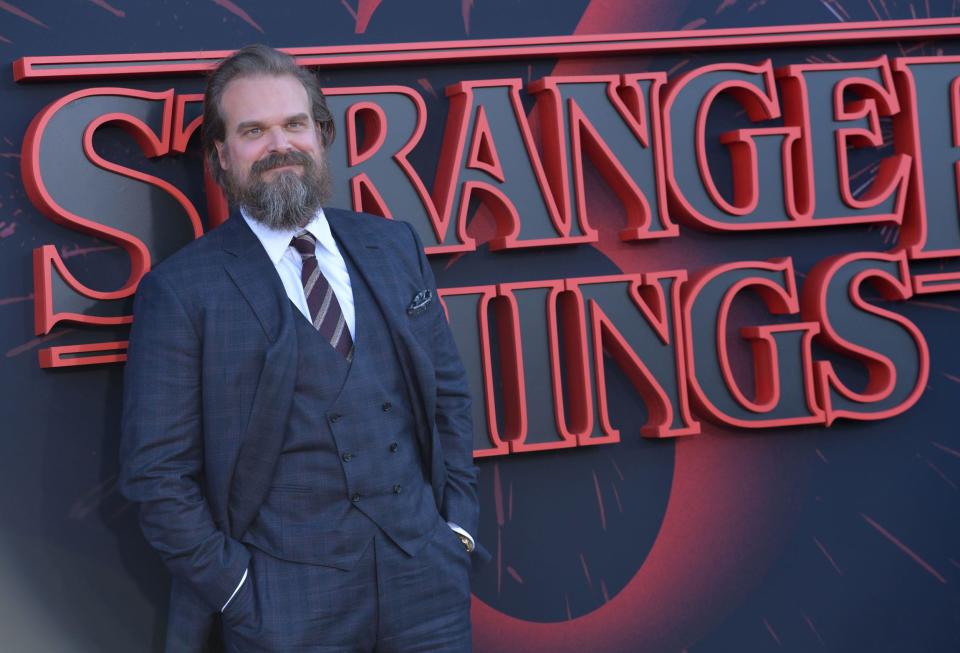 David Harbour in a suit next to a Stranger Things logo