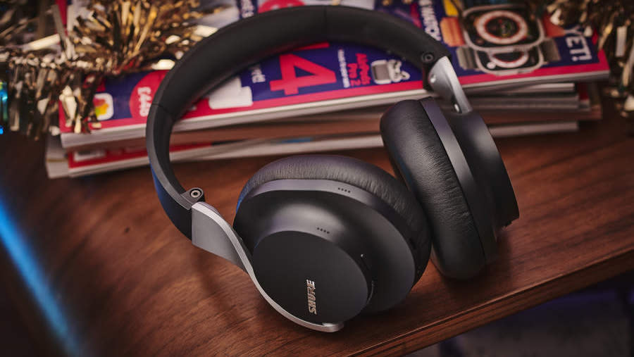 Set of headphones on a wooden table surrounded by magazines