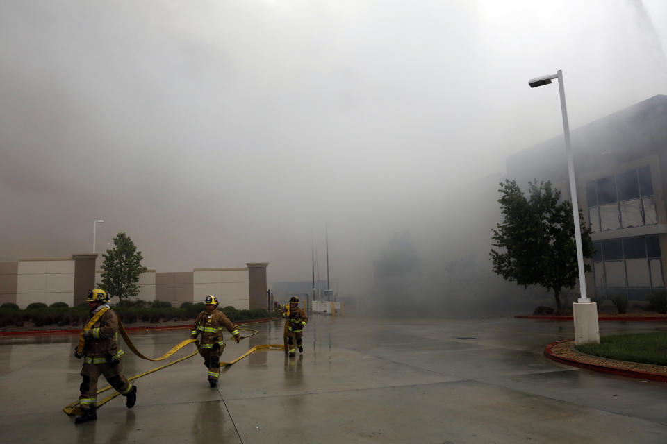 Firefighters carry a water hose as smoke from a burning warehouse fills the air Friday, June 5, 2020, in Redlands, Calif. The fire destroyed the commercial building, about 60 miles east of Los Angeles, but there are no reports of injuries. (AP Photo/Jae C. Hong)