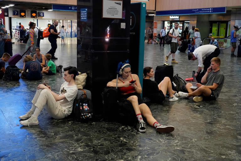 Los pasajeros de tren se sientan con sus pertenencias en la estación de tren de Euston en el centro de Londres, el 19 de julio de 2022, cuando los servicios se cancelaron debido a un incendio en la vía y el país experimenta una ola de calor extremo