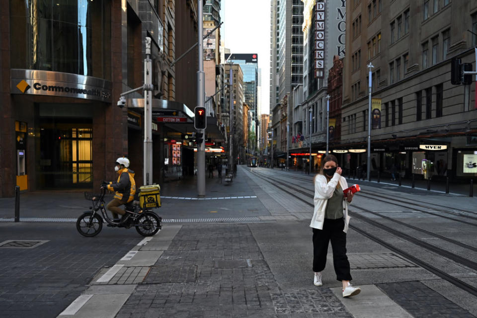 A woman crosses the street as a delivery rider drives past in the Sydney CBD, Australia.
