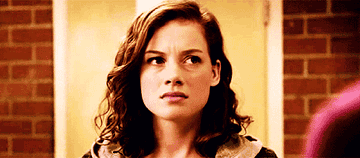 Jane Levy with a puzzled expression, in a scene from a TV show or movie. Background shows an indoor setting with brick walls