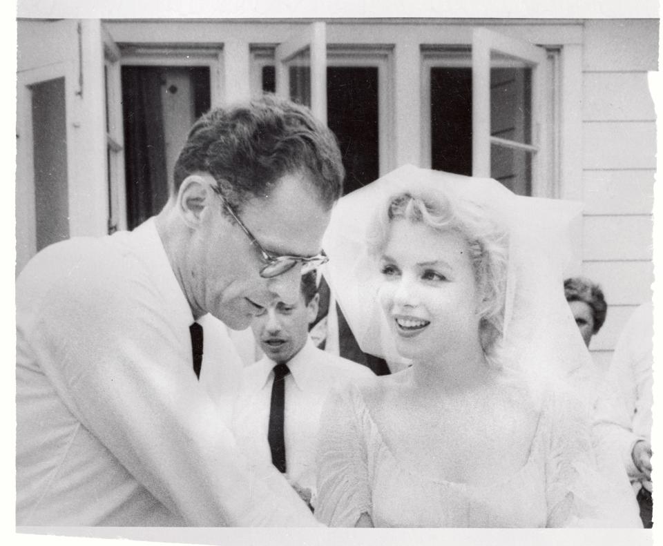 Marilyn Monroe, in a wedding dress and veil, looks at her husband, Arthur Miller, who looks down.