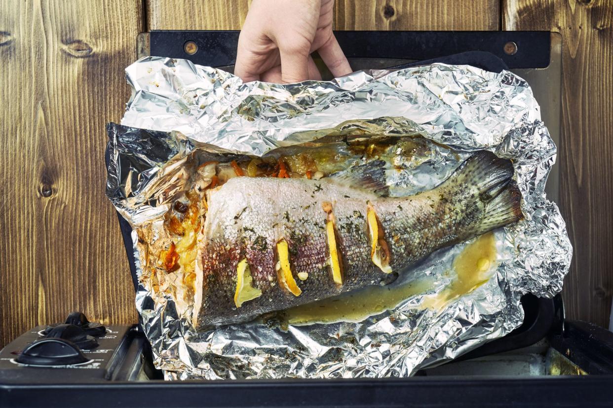 Girl taking out a freshly baked trout fish from an electric oven