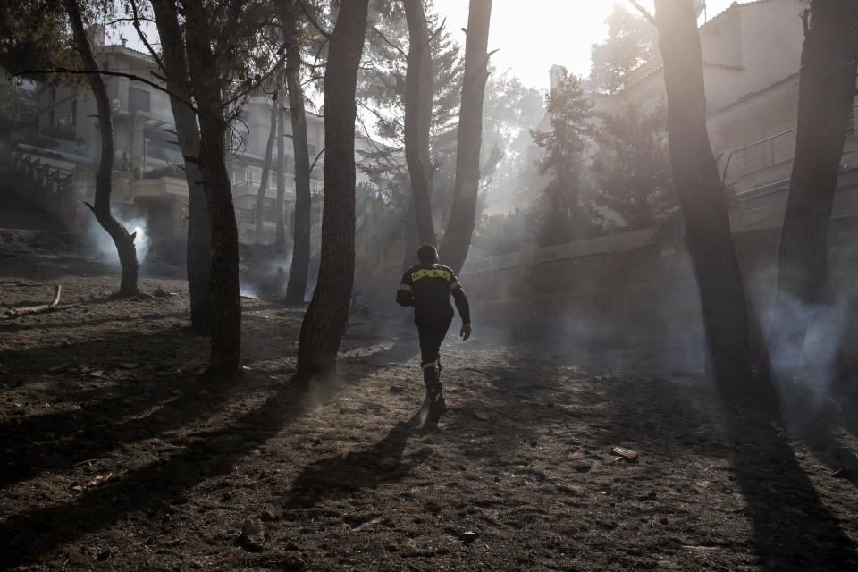 A firefighter makes his way through burnt trees following a forest fire at Dionysos northern suburb of Athens, on Tuesday, July 27, 2021. Greek authorities have evacuated several areas north of Athens as a wildfire swept through a hillside forest and threatened homes despite a large operation mounted by firefighters. (AP Photo/Yorgos Karahalis)