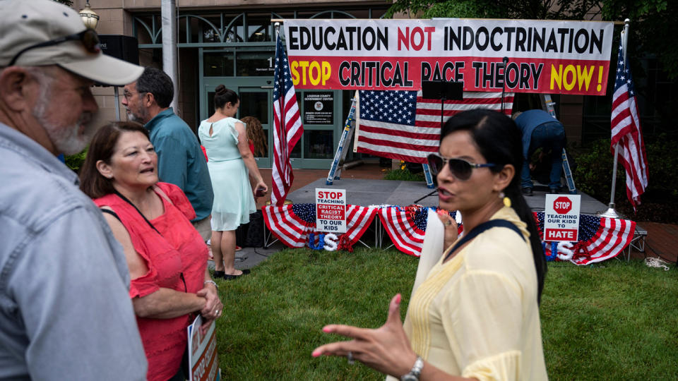 People talk before the start of a rally, with a sign in the background that reads, 