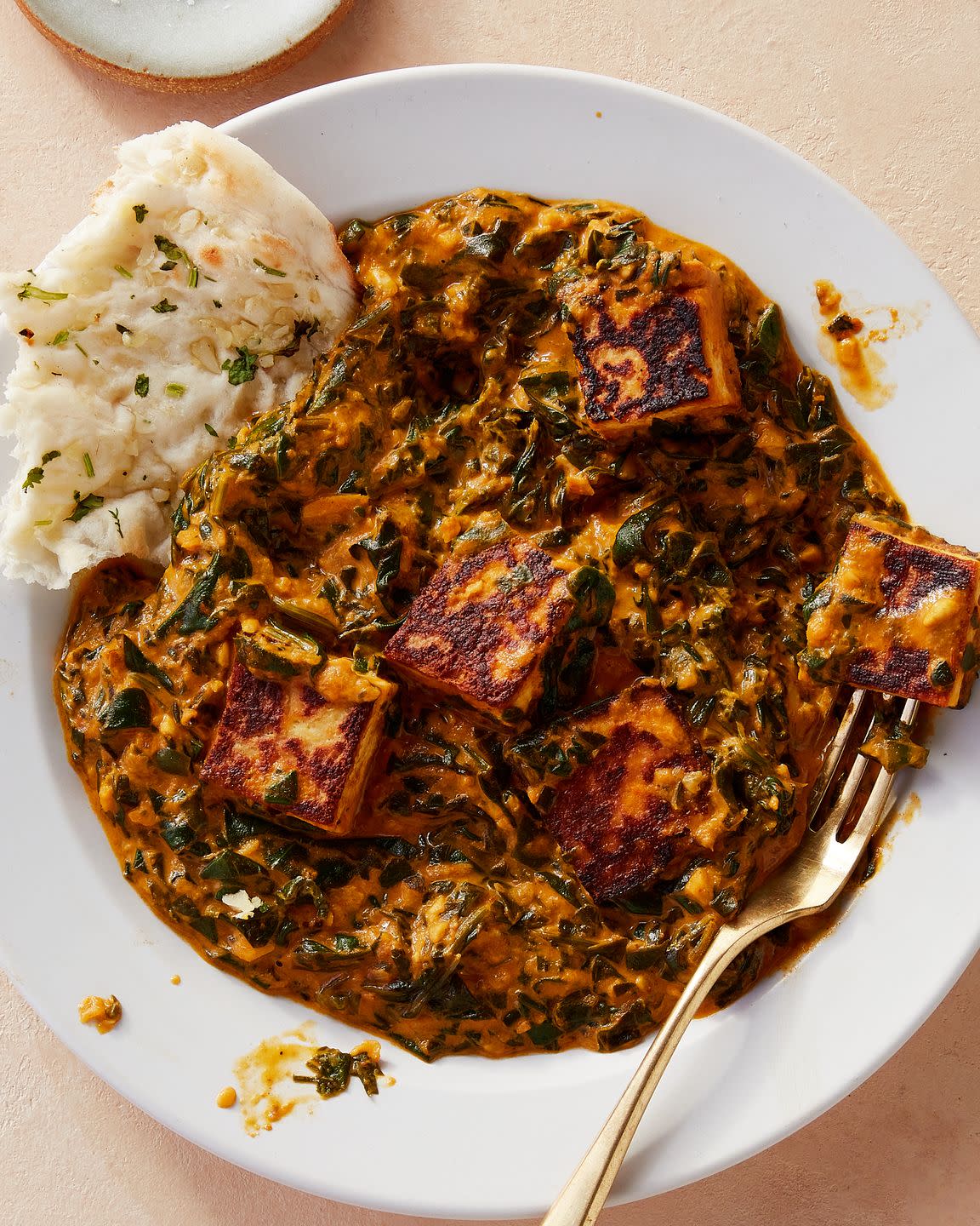 white bowl of saag paneer garnished with naan bread