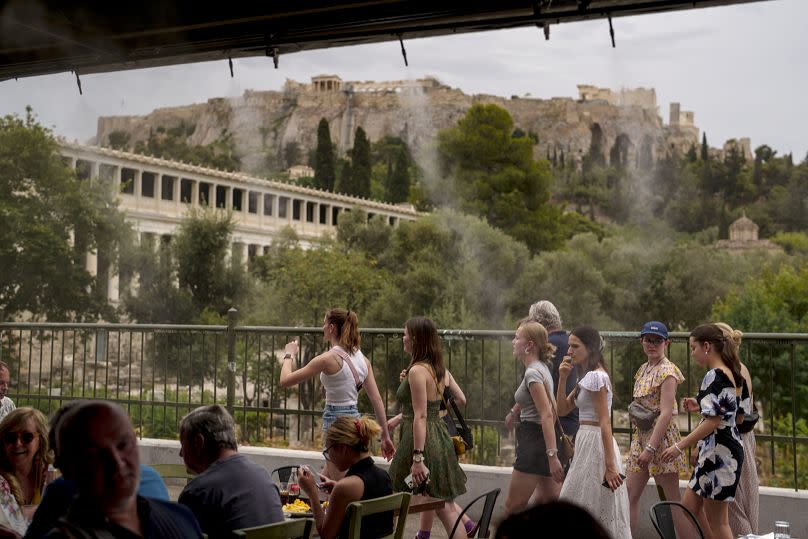 Des touristes marchent à côté d'un brumisateur dans le quartier de Monastiraki à Athènes, avec l'Acropole en fond, le jeudi 13 juin 2024