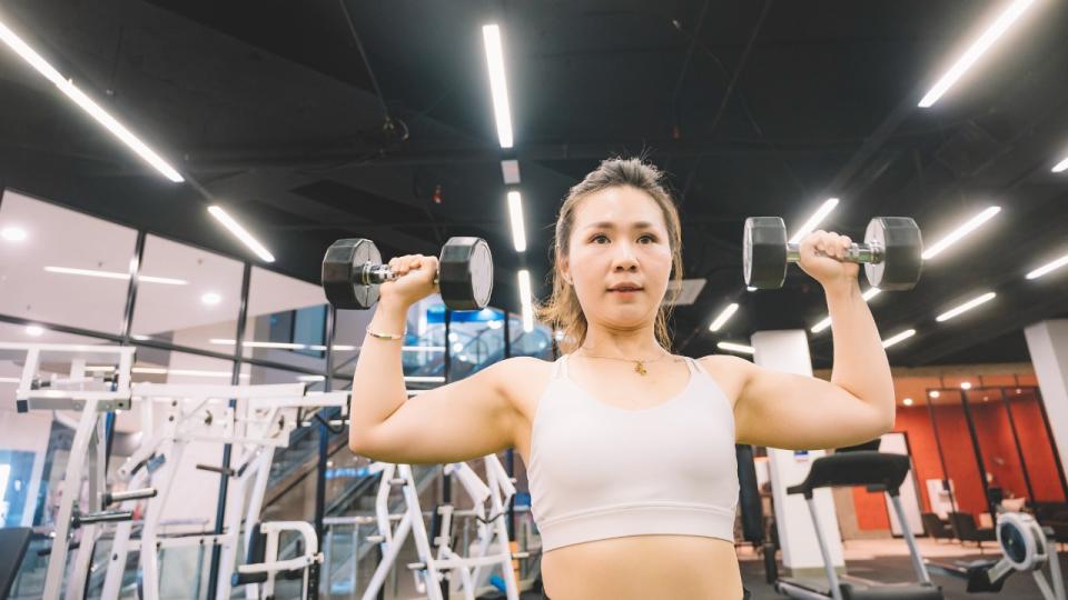 Woman performs overhead press exercise with dumbbells