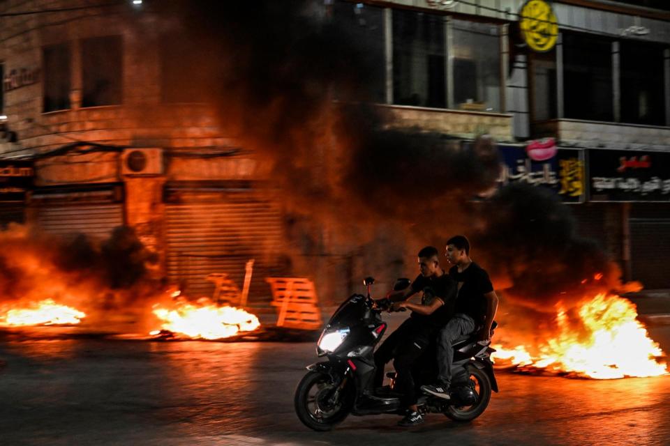 PHOTO: Palestinian youths ride past burning tyres during an Israeli raid on the occupied West Bank city of Jenin on May 21, 2024.  (Ronaldo Schemidt/AFP via Getty Images)