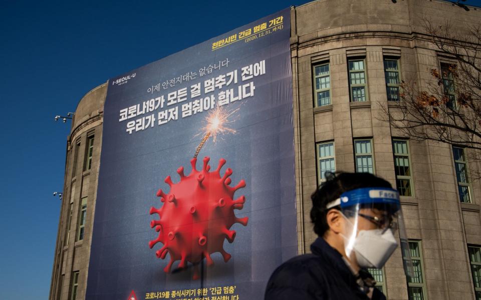 A pedestrian wearing a protective mask and face shield walks past a Covid-19 banner outside the Seoul Metropolitan Library in Seoul - Bloomberg