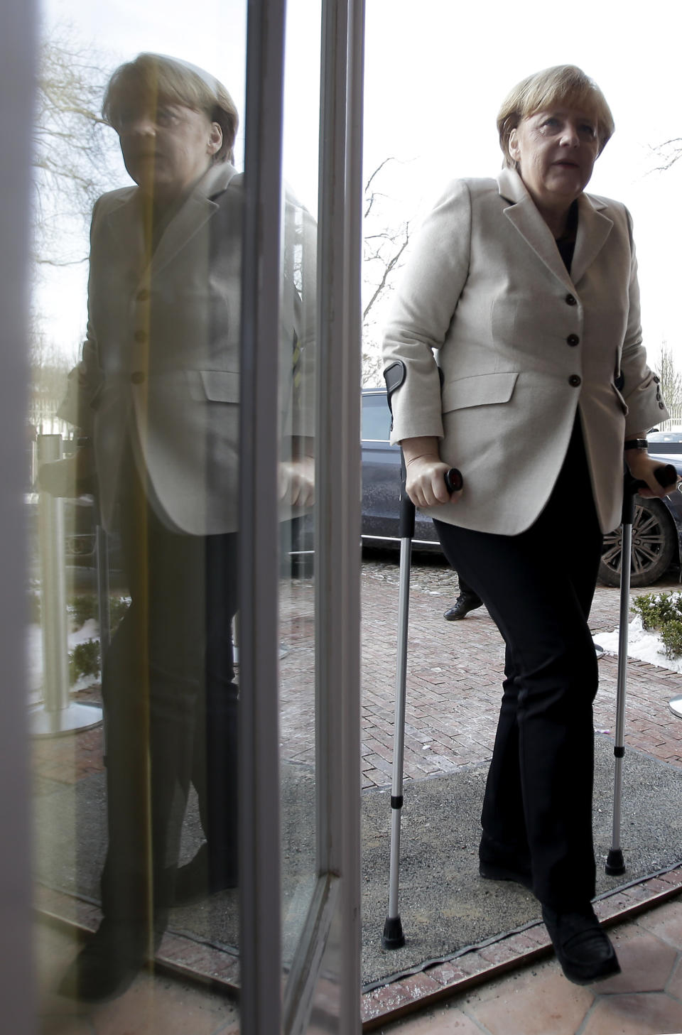 German Chancellor Angela Merkel is reflected in a glass door as she arrives for a press conference after a cabinet meeting as part of a two day closed meeting of the German government at the Meseberg palace near Berlin, Germany, Thursday, Jan. 23, 2014. Merkel uses crutches after a skiing accident. (AP Photo/Michael Sohn)