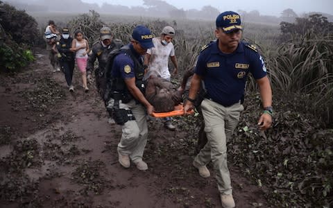 Police officers carry a wounded man after the eruption in El Rodeo village - Credit: NOE PEREZ/ AFP