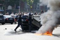 French riot police stand next to an overturned car as striking French taxi drivers demonstrate at the Porte Maillot to block the traffic on the Paris ring road during a national protest against car-sharing service Uber, in Paris, France, June 25, 2015. (REUTERS/Charles Platiau)