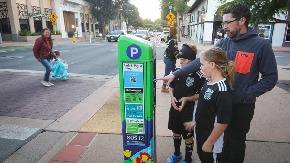 Jeff Andrews registers for parking on Marsh Street on Oct. 26, 2023, with help from kids Sebastian, left, and Emerson. Parking kiosks have replaced parking meters in San Luis Obispo’s downtown core, and parking fees are now paid via app or credit card.