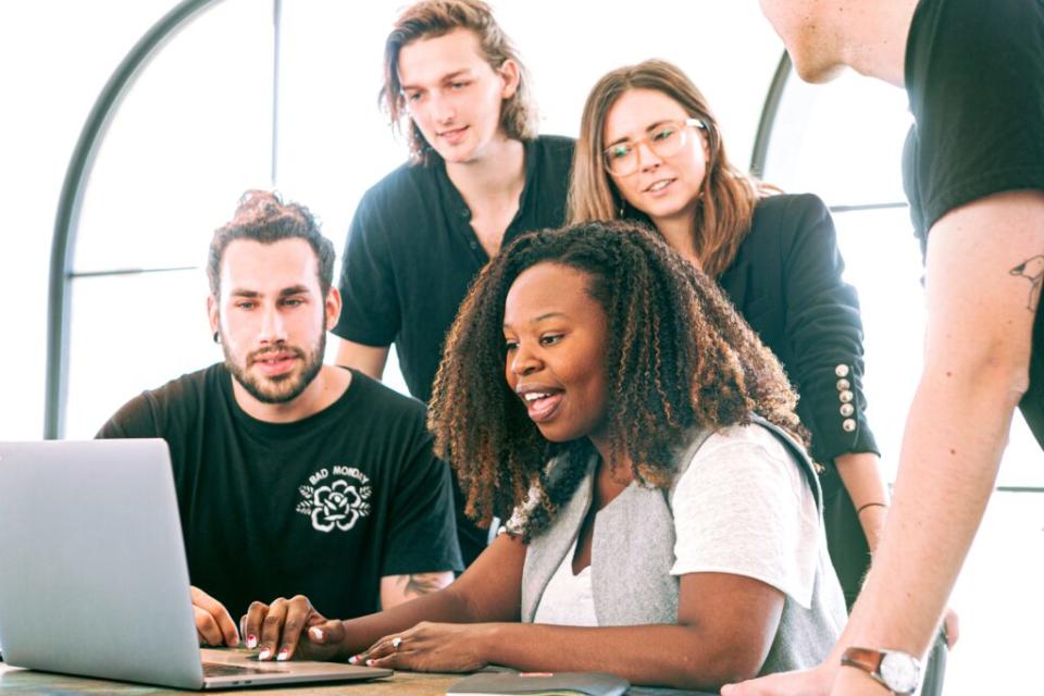 A Black woman sharing something on her laptop with her coworkers.