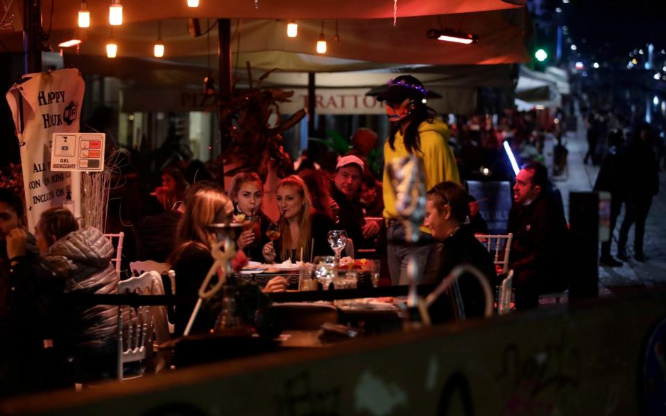 People have a drink and relax at the Naviglio Grande canal, one of the favorite spots for night life in Milan, Italy, Tuesday, Oct. 13, 2020. Italian Premier Giuseppe Conte says the aim of Italy's new anti-virus restrictions limiting nightlife and socializing is to head off another generalized lockdown. - Luca Bruno/AP Photo