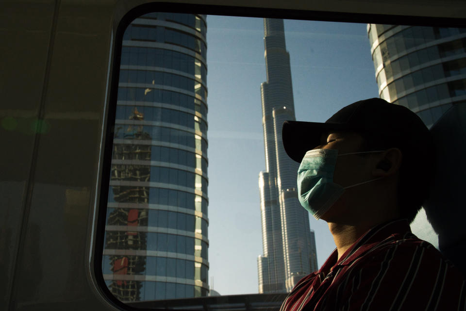 FILE - In this April 26, 2020 file photo, a commuter wearing a face mask to help curb the spread of the coronavirus, sleeps aboard the driverless Metro as it passes the Burj Khalifa, the world's tallest building, in Dubai, United Arab Emirates. Travel agencies in countries across the Middle East and Africa say the United Arab Emirates has temporarily halted issuing new visas to their citizens, a so-far unexplained ban on visitors amid both the coronavirus pandemic and as the UAE normalizes ties with Israel. (AP Photo/Jon Gambrell, File)